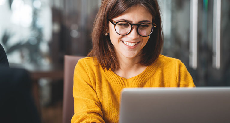 Woman with glasses smiling at laptop while working