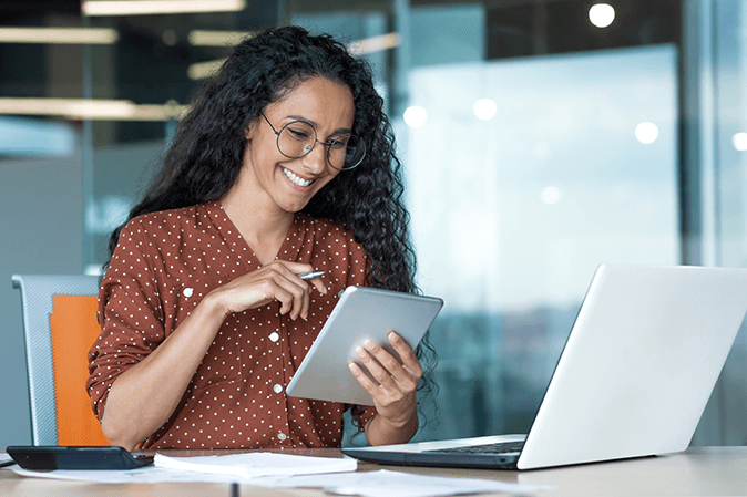 A businesswoman smiling while using a tablet device in front of a laptop 