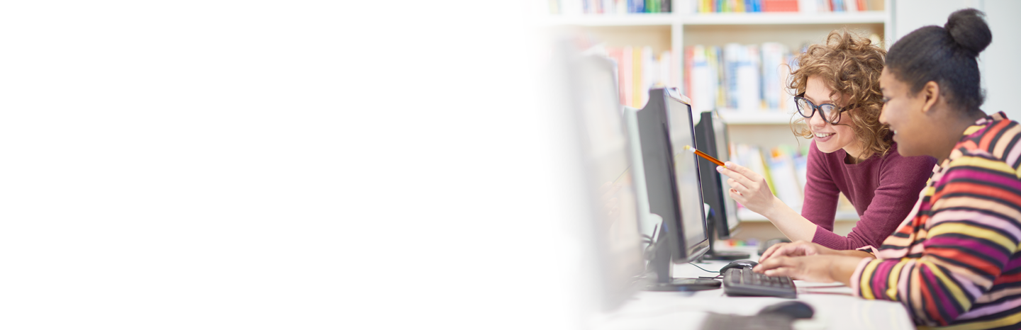 Young woman helping another woman on a computer in a library
